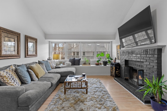 living area with high vaulted ceiling, a brick fireplace, and wood finished floors