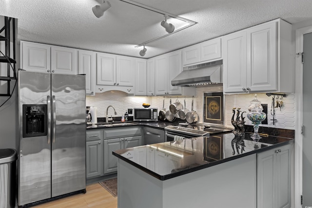 kitchen with a peninsula, appliances with stainless steel finishes, dark countertops, and under cabinet range hood