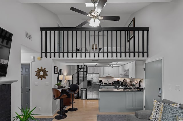 kitchen with light wood finished floors, dark countertops, a high ceiling, stainless steel fridge, and a peninsula