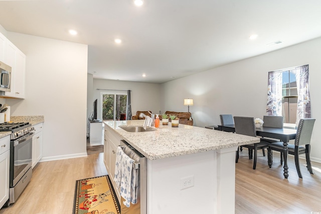 kitchen featuring a kitchen island with sink, a sink, white cabinetry, appliances with stainless steel finishes, and light wood-type flooring