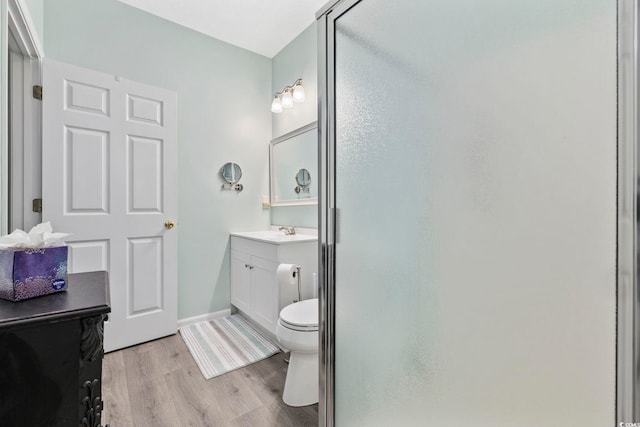 bathroom with toilet, wood finished floors, vanity, baseboards, and a shower stall