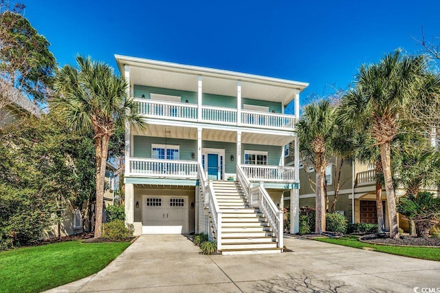 coastal home featuring an attached garage, a balcony, covered porch, driveway, and stairway