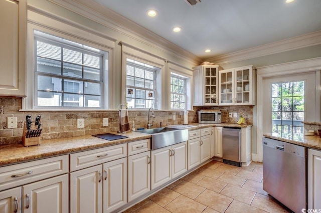 kitchen with appliances with stainless steel finishes, glass insert cabinets, white cabinetry, a sink, and light stone countertops