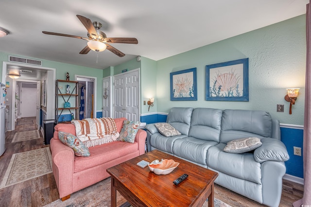 living room with a ceiling fan, visible vents, and wood finished floors