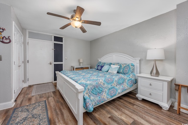 bedroom with dark wood-style floors, ceiling fan, a textured wall, and baseboards