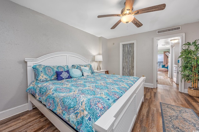 bedroom featuring a textured wall, dark wood-type flooring, visible vents, and baseboards