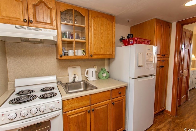 kitchen with light countertops, glass insert cabinets, a sink, white appliances, and under cabinet range hood