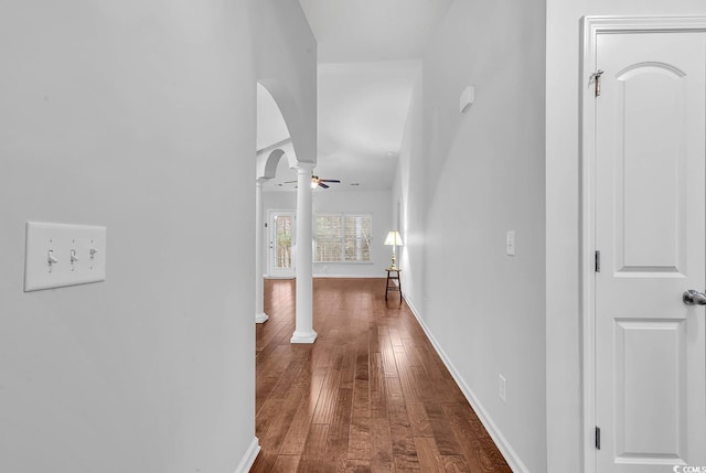 hall featuring dark wood-style floors, decorative columns, arched walkways, and baseboards