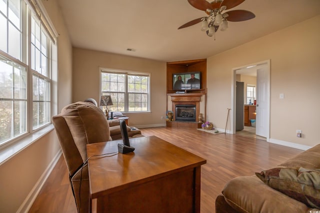 living area featuring a wealth of natural light, visible vents, wood finished floors, and a glass covered fireplace