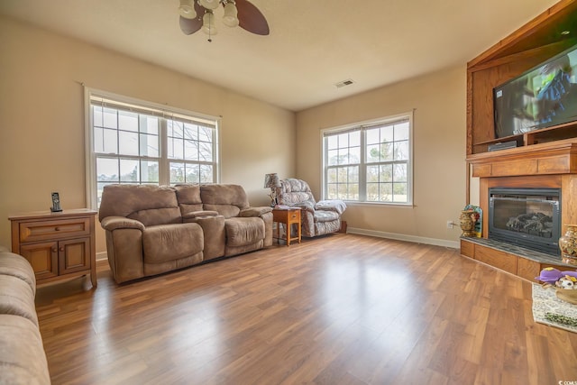 living room with a large fireplace, baseboards, visible vents, a ceiling fan, and wood finished floors