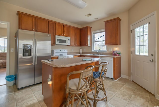 kitchen with white appliances, visible vents, a kitchen island, brown cabinets, and light countertops