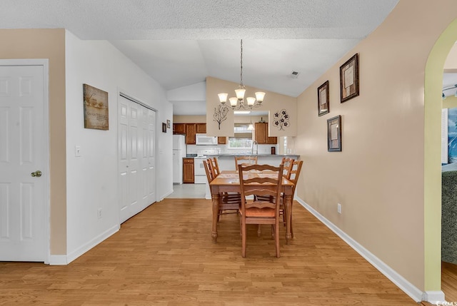 dining area featuring arched walkways, an inviting chandelier, vaulted ceiling, a textured ceiling, and light wood-style floors