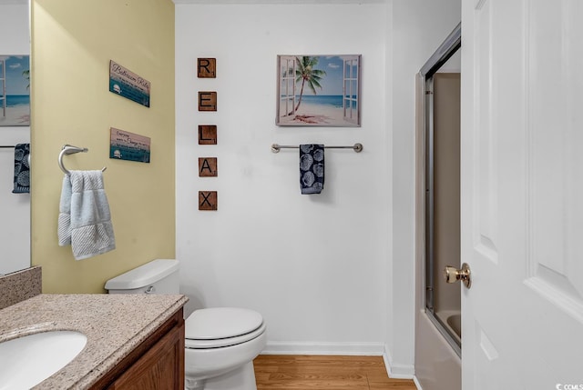 full bathroom with shower / bath combination with glass door, vanity, toilet, wood finished floors, and baseboards
