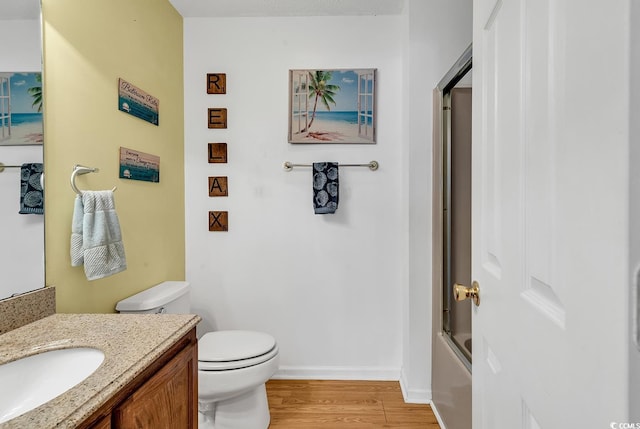 bathroom with baseboards, bath / shower combo with glass door, toilet, wood finished floors, and vanity