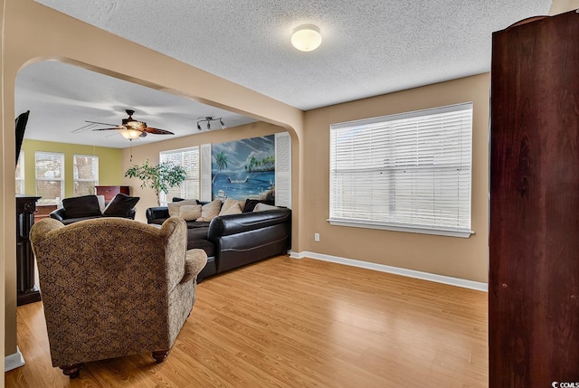 living room featuring arched walkways, a textured ceiling, a ceiling fan, baseboards, and light wood-type flooring