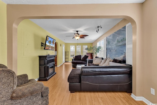 living room featuring a ceiling fan, arched walkways, light wood-style flooring, and baseboards