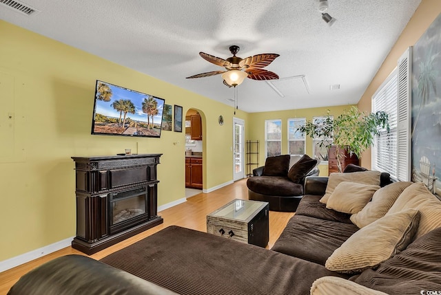living room with light wood-style floors, attic access, ceiling fan, and visible vents