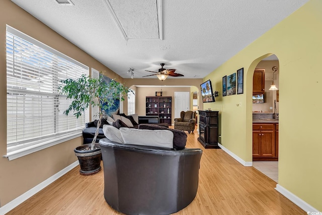 living area featuring attic access, light wood-style flooring, a textured ceiling, and a ceiling fan