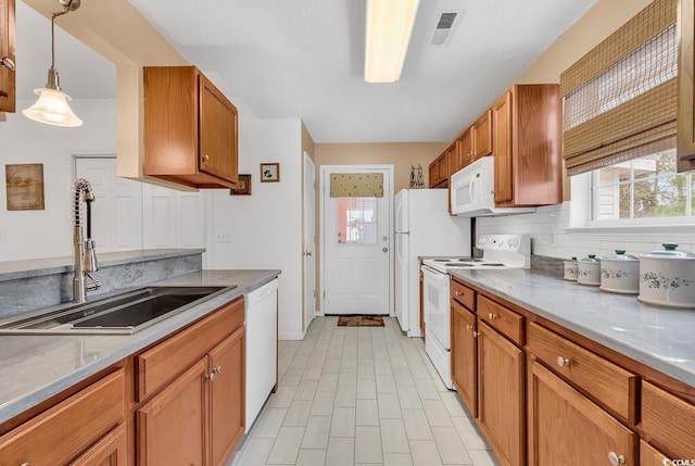 kitchen featuring white appliances, brown cabinets, a sink, and decorative light fixtures