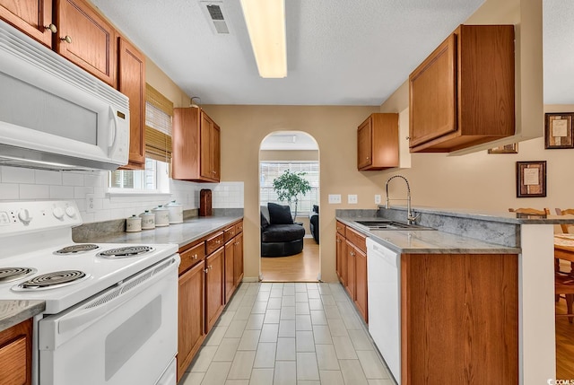 kitchen with arched walkways, white appliances, visible vents, light countertops, and brown cabinetry