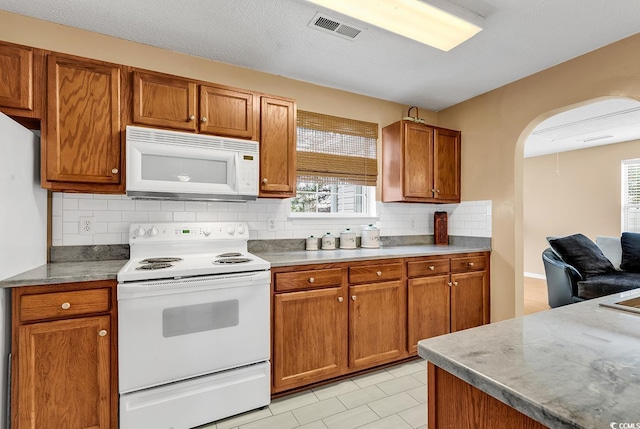 kitchen featuring white appliances, backsplash, visible vents, brown cabinets, and arched walkways