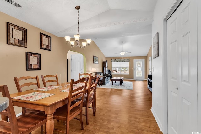 dining space with arched walkways, ceiling fan with notable chandelier, wood finished floors, visible vents, and vaulted ceiling