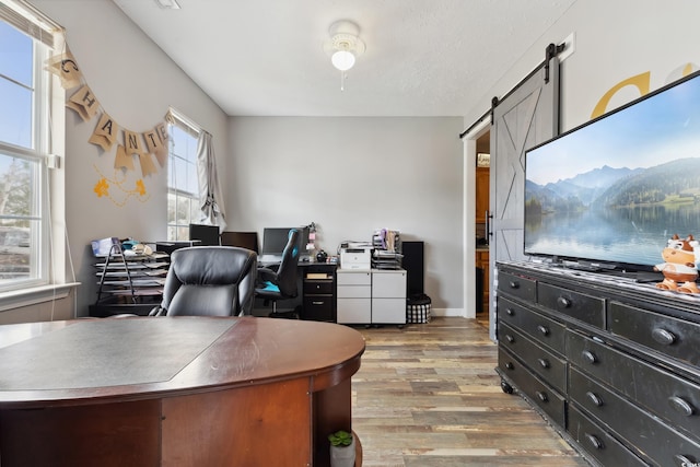 home office with a barn door, wood finished floors, and baseboards