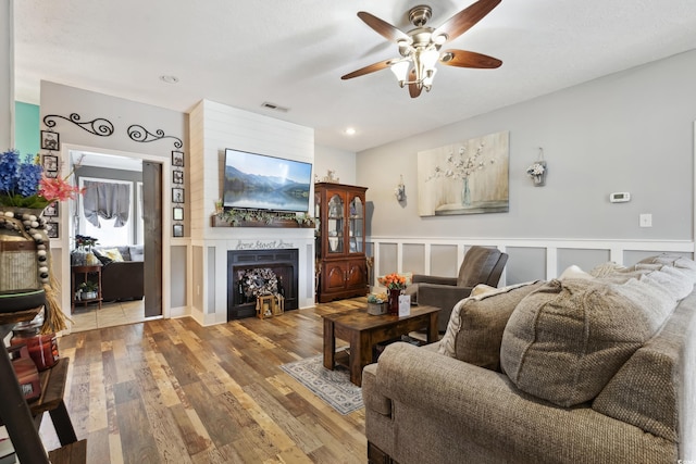 living room with visible vents, a wainscoted wall, wood finished floors, a fireplace, and a decorative wall