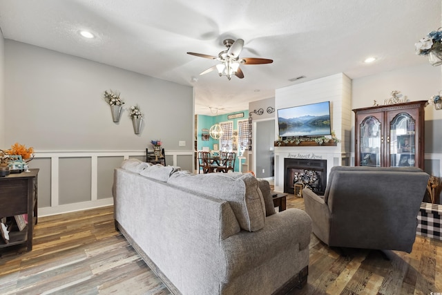 living room with a wainscoted wall, a fireplace, a decorative wall, a ceiling fan, and wood finished floors