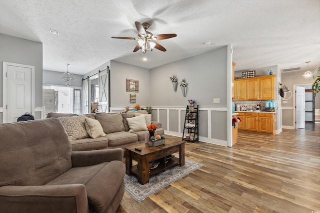 living room featuring a textured ceiling, a barn door, a ceiling fan, visible vents, and light wood finished floors