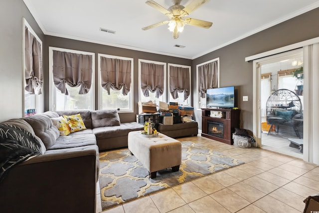 living room featuring a glass covered fireplace, visible vents, crown molding, and tile patterned floors