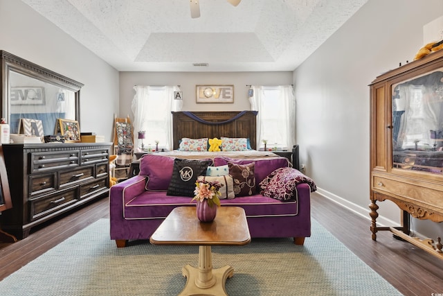 bedroom with baseboards, ceiling fan, wood finished floors, a tray ceiling, and a textured ceiling