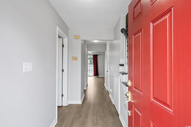 corridor featuring a textured ceiling, wood finished floors, and baseboards