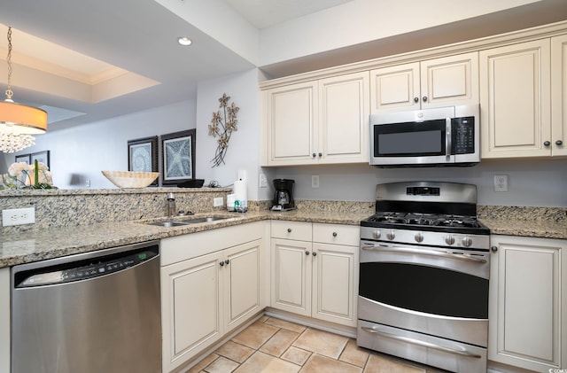 kitchen featuring light stone counters, hanging light fixtures, appliances with stainless steel finishes, a sink, and a peninsula