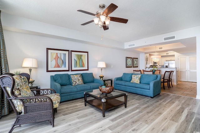 living area featuring ceiling fan, light wood finished floors, a textured ceiling, and visible vents