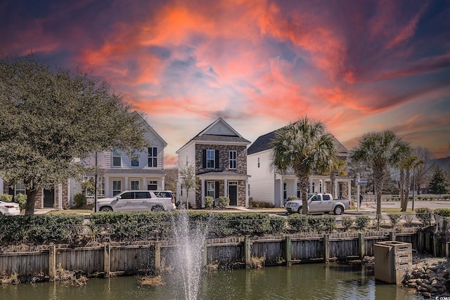 back of house at dusk with stone siding and a water view