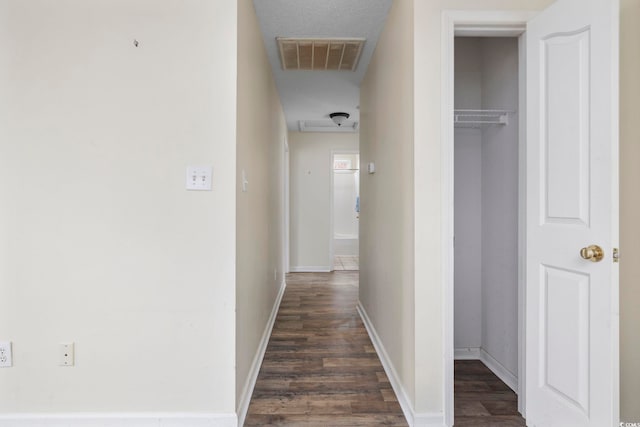 hallway with dark wood-style flooring, visible vents, and baseboards