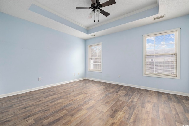 empty room featuring a tray ceiling, a textured ceiling, baseboards, and wood finished floors