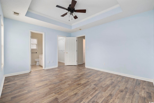 unfurnished bedroom with a spacious closet, wood finished floors, a raised ceiling, and baseboards