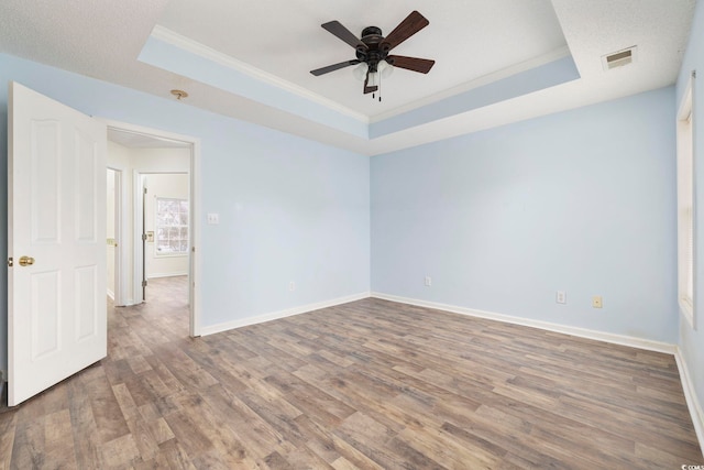 spare room with a raised ceiling, visible vents, ornamental molding, wood finished floors, and baseboards