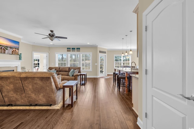 living area featuring crown molding, a fireplace, dark wood finished floors, ceiling fan, and baseboards