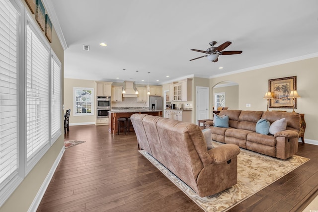 living area with arched walkways, visible vents, baseboards, ornamental molding, and dark wood-style floors