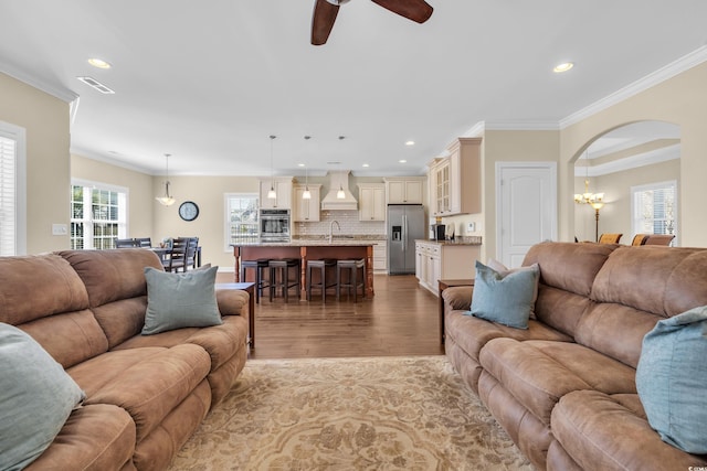 living room with arched walkways, recessed lighting, visible vents, light wood-style flooring, and ornamental molding