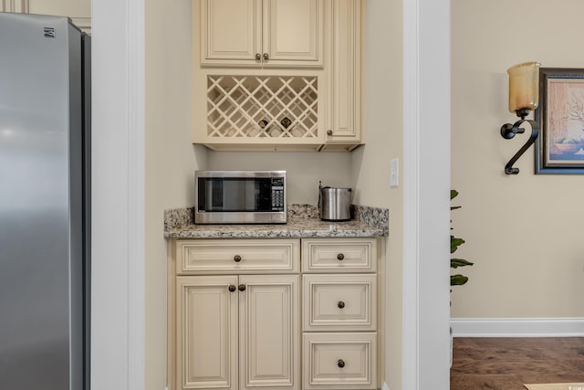 kitchen featuring baseboards, appliances with stainless steel finishes, cream cabinetry, and light stone countertops