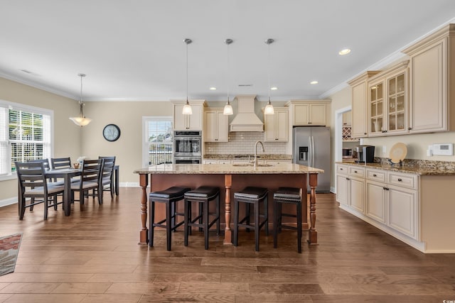 kitchen with custom exhaust hood, cream cabinets, glass insert cabinets, and hanging light fixtures