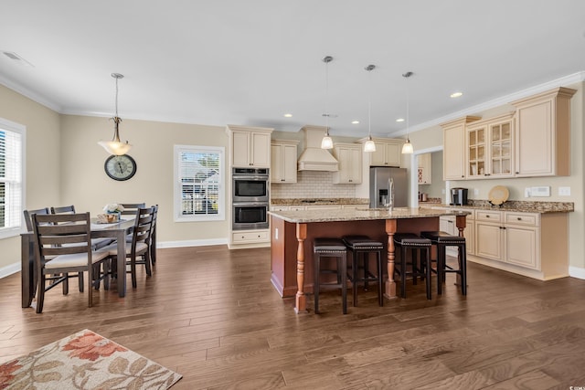 kitchen featuring a breakfast bar, hanging light fixtures, glass insert cabinets, appliances with stainless steel finishes, and an island with sink