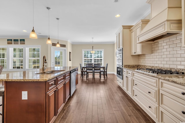 kitchen featuring stainless steel appliances, decorative light fixtures, an island with sink, and custom exhaust hood