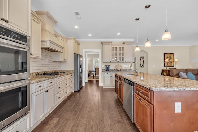 kitchen featuring appliances with stainless steel finishes, glass insert cabinets, open floor plan, pendant lighting, and a sink