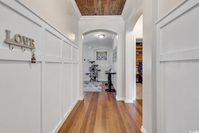 corridor with arched walkways, baseboards, wood finished floors, and crown molding