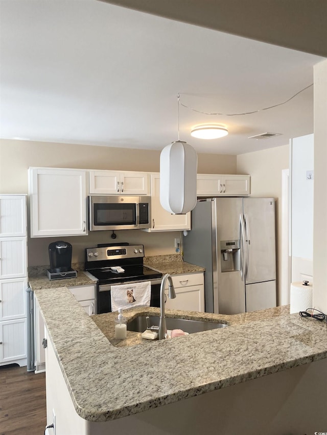 kitchen with light stone counters, a peninsula, stainless steel appliances, white cabinetry, and a sink